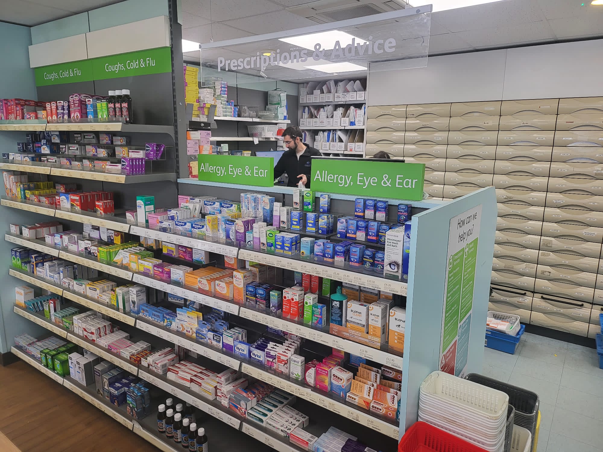 Inside Midsomer Pharmacy showing all the OTC medicines displayed on the shelves plus you can see a partial view of the back dispensary where prescription medicine is prepared for patients